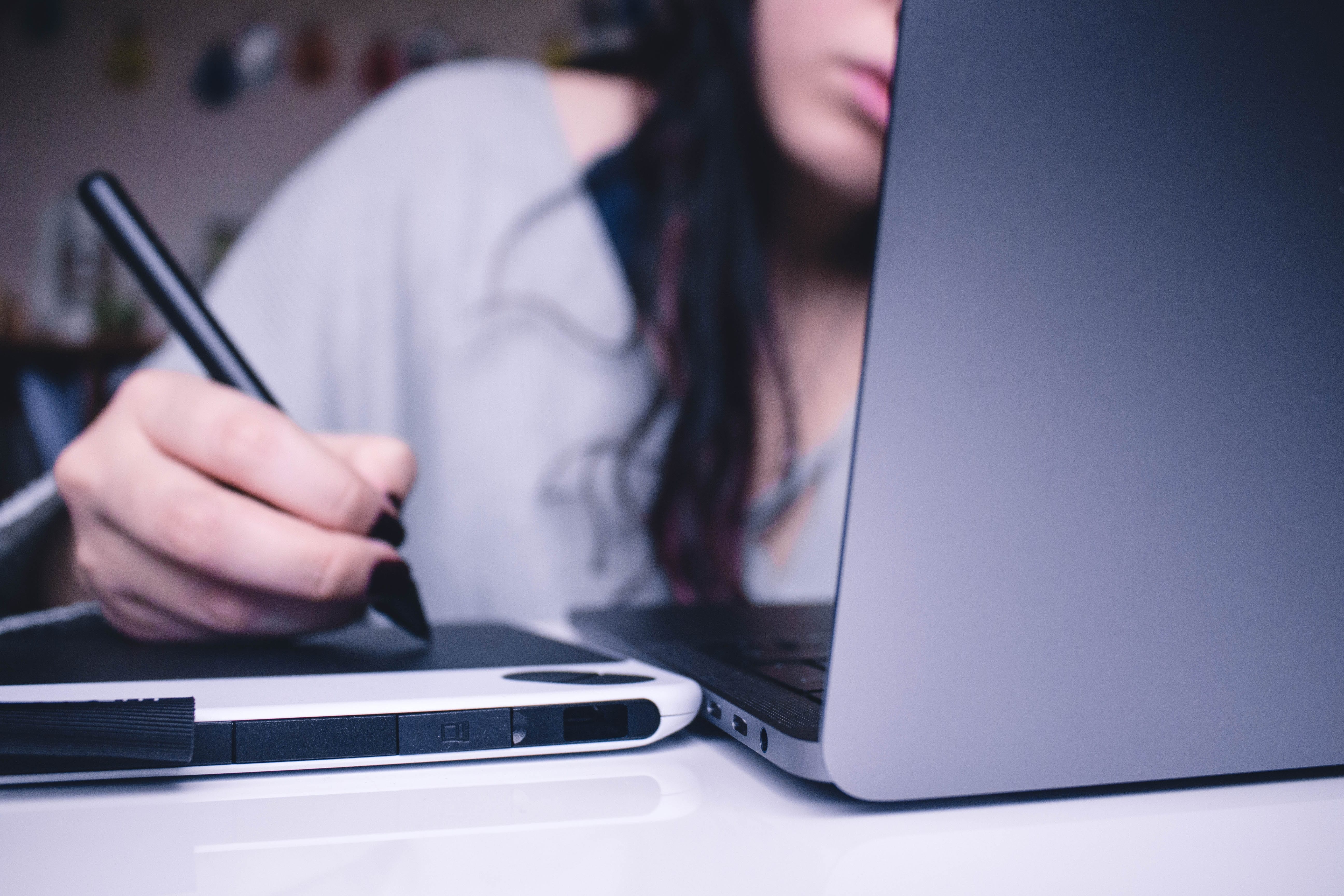 A woman sitting at a laptop and using a drawing tablet