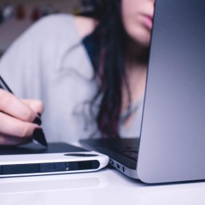 A woman sitting at a laptop and using a drawing tablet